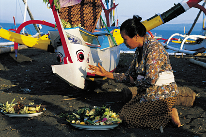 Sur lle de Bali, les offrandes font partie de la vie quotidienne. Ici, une femme en dpose devant un bateau dont la proue reprsente un poisson-lphant, afin de protger les marins.